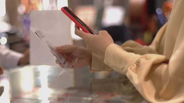 An upwardly mobile Asian Muslim woman using a Smartwatch to pay for a product at a sale terminal with nfc identification payment for verification and authentication