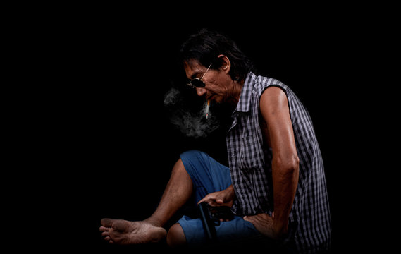 The portrait slim old Asia man was smoking and holding a gun at the black background, Image of cigarette smoke spread in the mouth concept