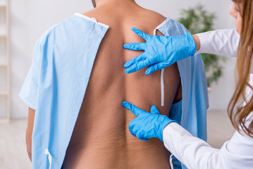 Young back injured man visiting female doctor chiropractor