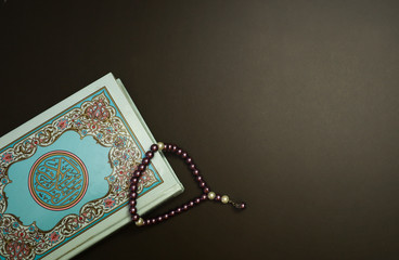 Holy Quran and prayer beads isolated on a dark wooden table.  Religious concept 