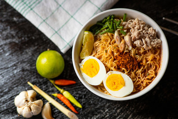 Spicy instant noodles soup with ingredient in bowl on wood black background