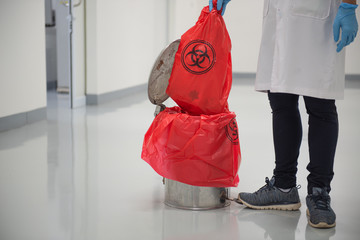 The cleaning staff is taking out the infected waste bags marked with the biohazard sign  to get rid...