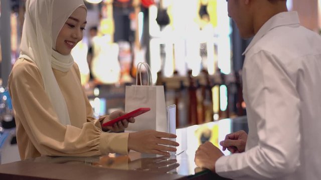 An upwardly mobile Asian Muslim woman using a Smartwatch to pay for a product at a sale terminal with nfc identification payment for verification and authentication