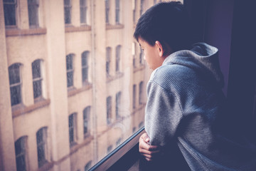 Fototapeta na wymiar Sad Asian preteen boy feeling lonely, looking out of window from his room, social distancing, isolation, mental health concept