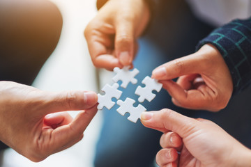 Closeup image of a group of people holding and putting a piece of white jigsaw puzzle together