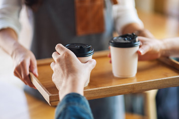 A waitress holding and serving paper cups of hot coffee to customer in cafe