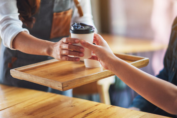 A waitress holding and serving paper cups of hot coffee to customer in cafe