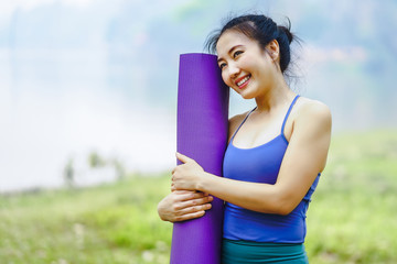 Young asian woman wearing exercise suit with yoga mat or fitness mat after practicing yoga in park. Healthy and Fitness concept
