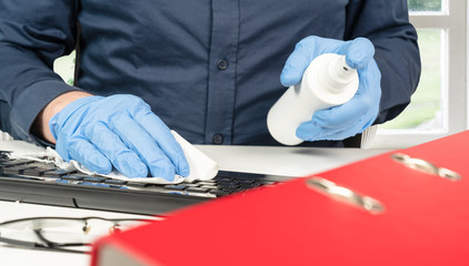 person cleans the office keyboard with a disinfectant