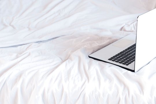 home office in a bed. white and black laptop on white crumpled sheets
