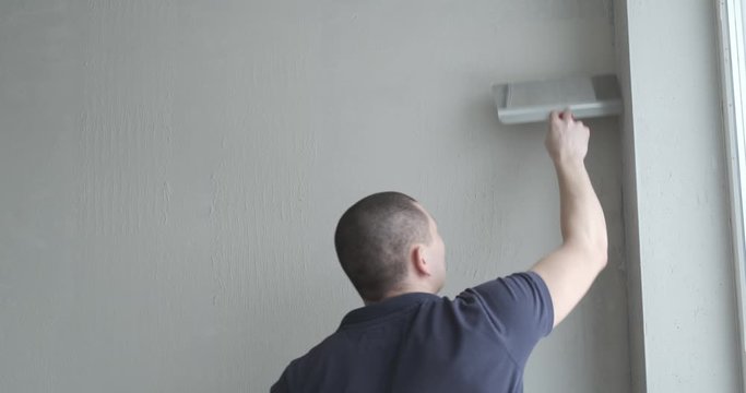 Young professional builder smooths wall with spatula. Putty put on leveled surface of wall. White putty of wall lines. Repairman does job efficiently. Smooth wall texture. Repair in own apartment.