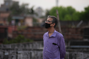 Portrait of an Indian old man with corona preventive mask on a rooftop  in home isolation.Indian lifestyle, disease and home quarantine.