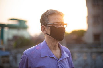 portrait of an Indian old man with corona preventive mask on a rooftop during sunset in home isolation.Indian lifestyle, disease and home quarantine.