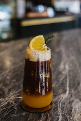 Fusion coffee, Iced orange juice and passion fruit mix black cold brew coffee in glass decorated with orange slice on Mable table. Summer drink blurred background.