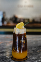 Fusion coffee, Iced orange juice and passion fruit mix black cold brew coffee in glass decorated with orange slice on Mable table. Summer drink blurred background.