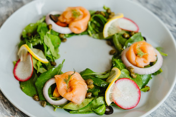 Smoked salmon salad with fresh vegetable spinach, lemon, beetroot slide, rocket, romaine lettuce in white dish on Mable table. tasty and healthy meal Concept.