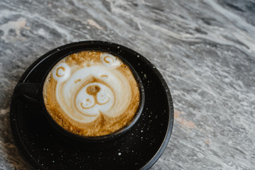 Top view teddy bear face latte art coffee shape in black cup on Mable background. Beverage menu in coffeeshop with copy space.