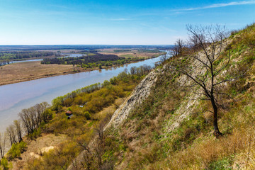 Fototapeta na wymiar Top view of the bend of the river, two banks, bare branches against the blue sky on a spring day