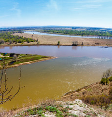 Top view of the bend of the river, two banks, bare branches against the blue sky on a spring day