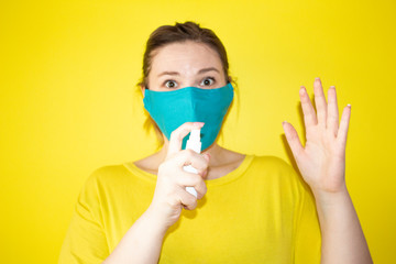 Portrait of young woman in protective mask with sanitizer gel on  yellow background. Coronavirus and health self isolation care concept.