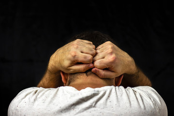 A man in a white T-shirt holds his hands behind his head. Closeup on black background. Back view.