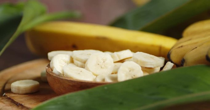 Slices of fresh banana on the plate with the leaves slowly rotate. On a wooden table.