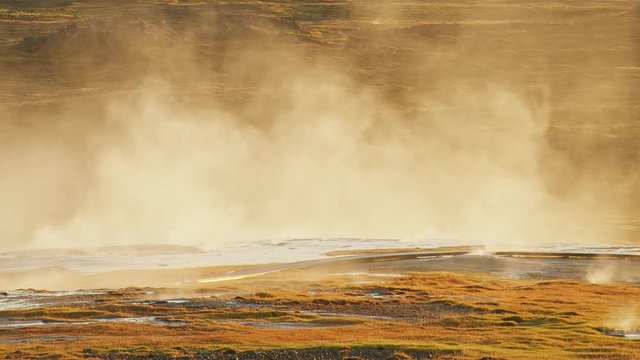 Hot steam rising from the golden ground of Iceland due to magma underground - wide shot