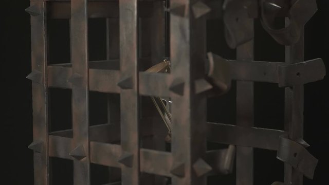 An hourglass is suspended in a rusty metal cage. With running time.