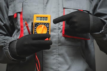 A multimeter in electrician worker hand close up on gray background.
