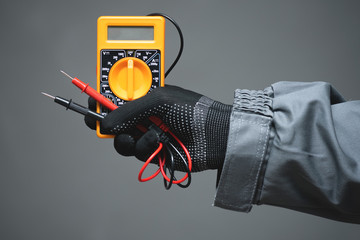 A multimeter in electrician worker hand close up on gray background.
