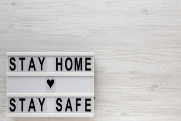 'Stay home stay safe' words on a lightbox on a white wooden surface, top view. Overhead, from above, flat lay. Copy space.