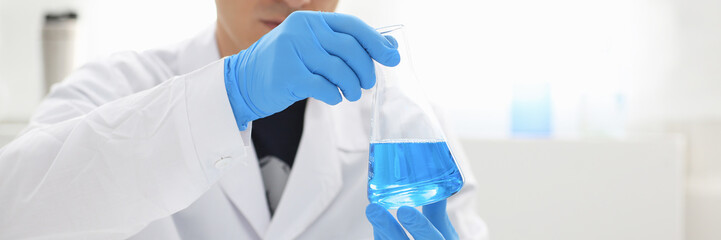 A male chemist holds test tube of glass in his hand overflows a liquid solution of potassium...
