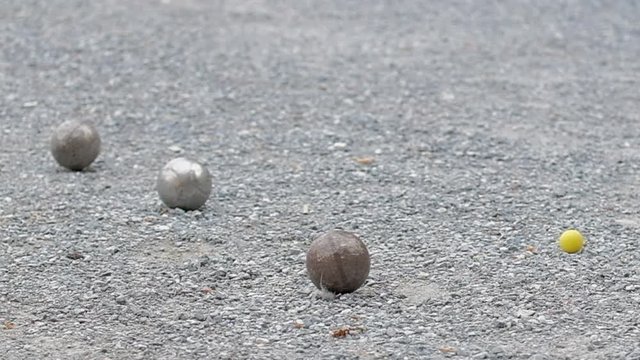 Close up of petanque boules and a yellow jack on the gravel ground.