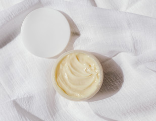 A top view of a organic cosmetic cream for face or body on white muslin tissue. Close-up. Natural lighting. Sunlight. Scin care concept.