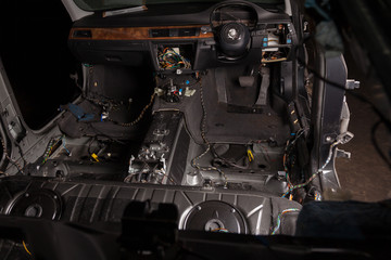 Car interior in the back of a sedan with a disassembled dashboard and view on steering wheel during preparation in a vehicle repair workshop. Auto service industry