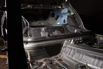 The rear body interior part of the cabin inside the sedan car, dismantled trim with colored wires, prepared for the replacement and installation of noise insulation in auto service for tuning vehicles