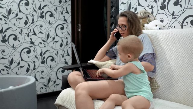 The girl works at home for her laptop. She talks on her cell phone. Her son keeps her from working.