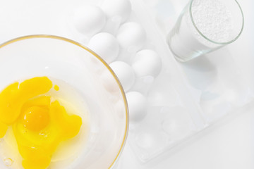 Yellow yolk with broken egg protein in a deep plate next to a pack of a dozen eggs and flour before cooking on a white isolated background.