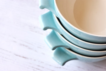 Closeup of a stack of light blue ceramic retro bowls from the 50s on a white painted wooden table with copy space. 