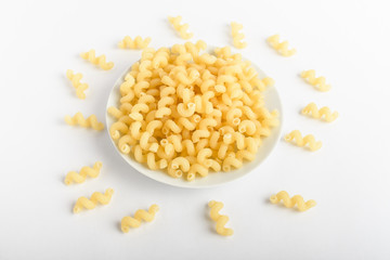 Dried serpentelli Italian pasta in a round bowl ready to be cooked, isolated on a white table, top view or flat lay of healthy food 
