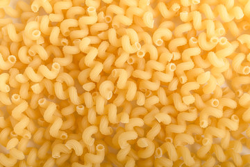 Heap of dried serpentelli Italian pasta in a round bowl ready to be cooked, isolated on a white table, top view or flat lay of healthy food 
