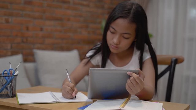 pretty asian teenager doing homework at home using tablet pc