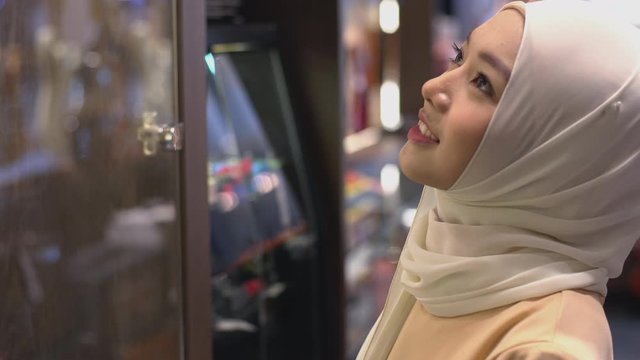 Close Up Portrait of a Young Asian Muslim Woman dressing in the traditional Hijab looking at shop window searching for the product