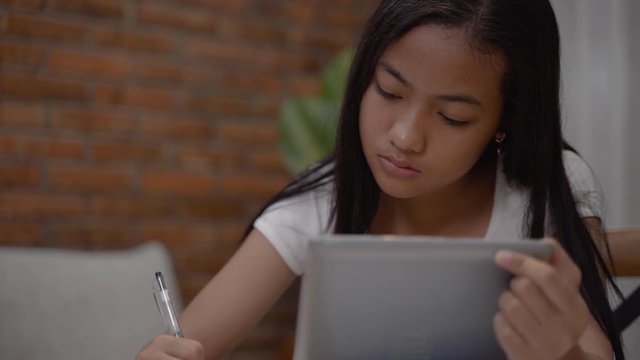 pretty asian teenager doing homework at home using tablet pc