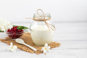 Obraz na płótnie Canvas Homemade yogurt in a glass jar on a wooden light background with a ceramic spoon. Healthy diet food. Vegetarian food.