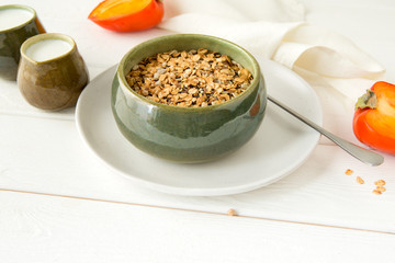 healthy breakfast concept, granola in a ceramic bowl, yogurt in jugs and persimmons on a light...
