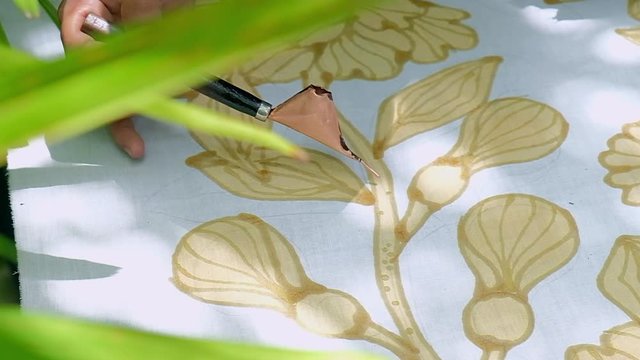 Close up of hand drawing traditional batik pattern with hot wax using canting tool.