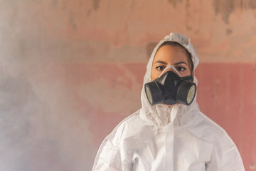 Young virologist doctor woman wearing a white biohazard protection suit and and a gas mask during...