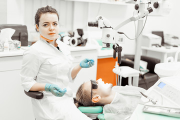 Dentist young woman treats a patient a man. The doctor uses disposable gloves, a mask and a hat. The dentist works in the patient's mouth, uses a professional tool.