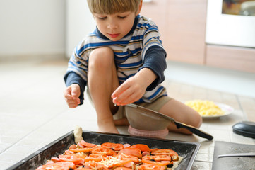 happy family make food at home. four year old toddler kid son helps his mother cooking pizza in the kitchen. concept pastimes of isolation time in quarantine mode during coronavirus covid-19